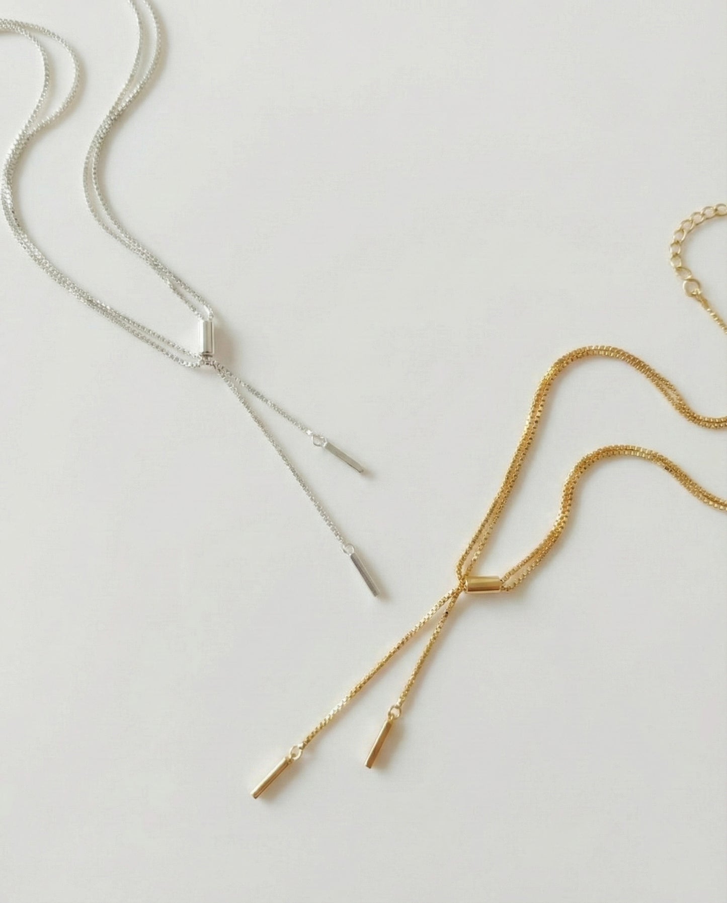 Double row Y-drop stick chain necklaces in silver and gold, laid flat on a white background