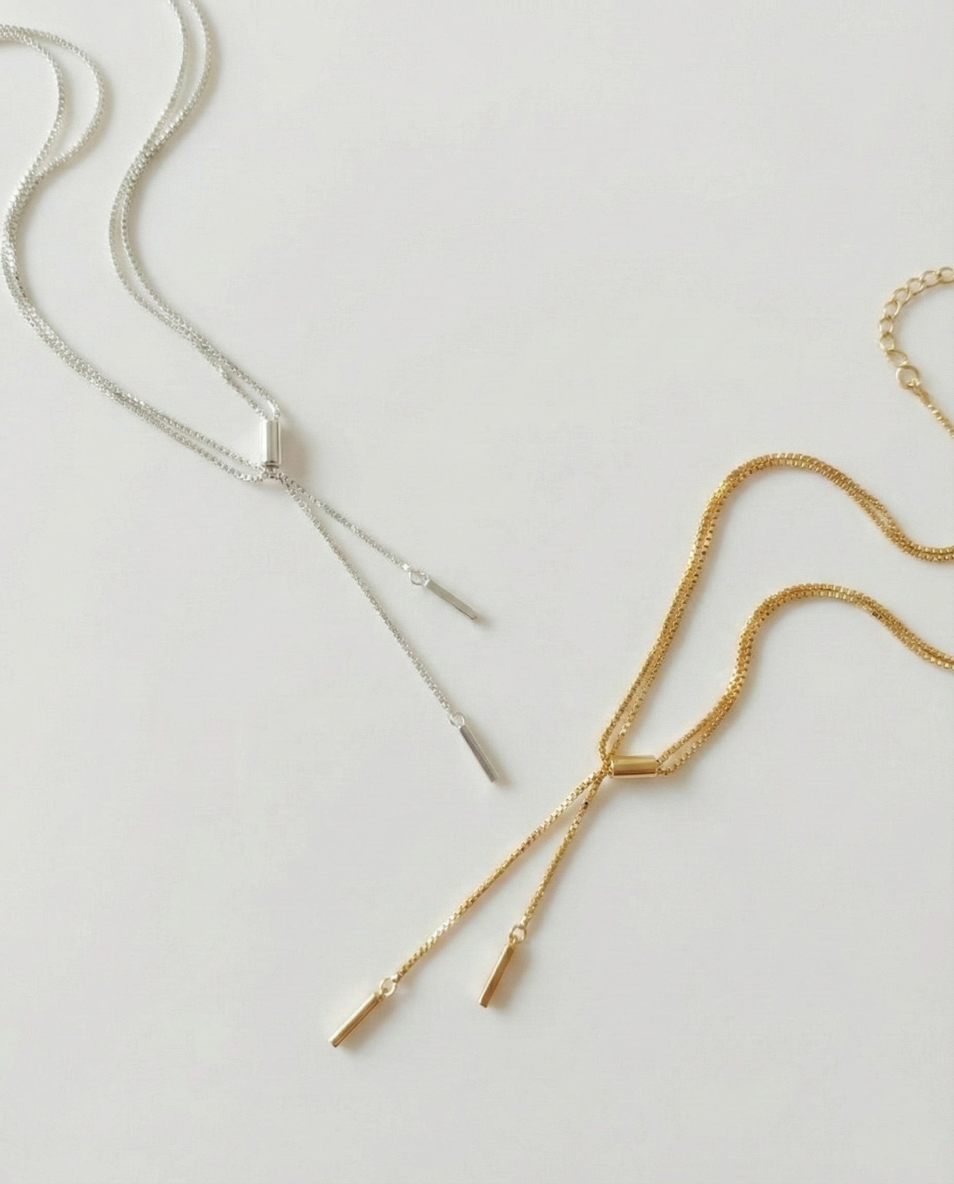 Double row Y-drop stick chain necklaces in silver and gold, laid flat on a white background