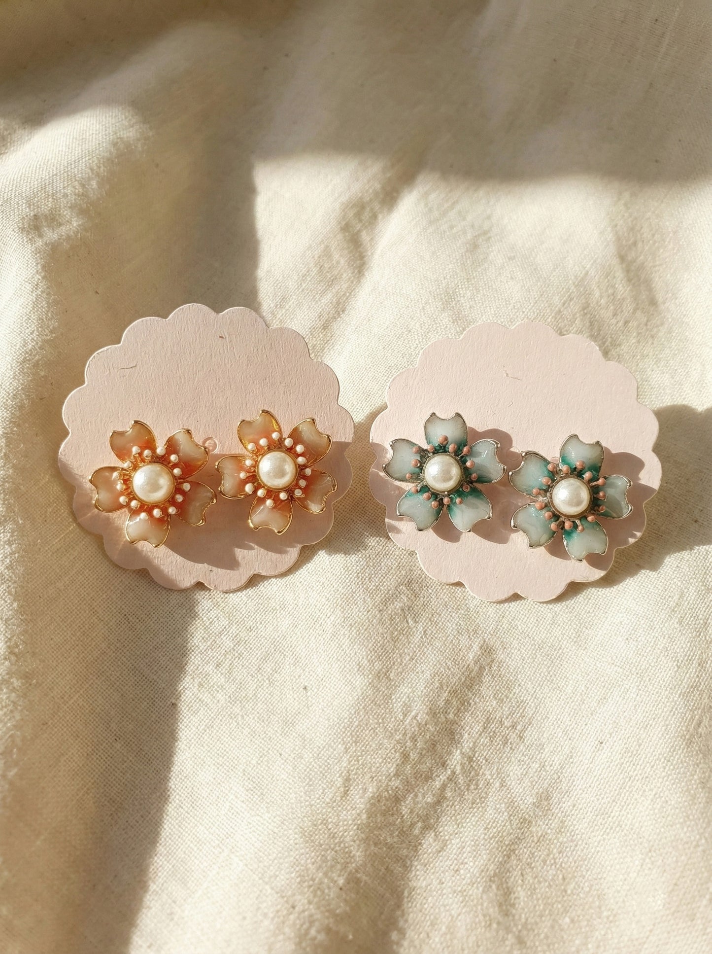 Two pairs of handmade Korean vintage flower earrings in mint green and peach coral on cream fabric with natural lighting