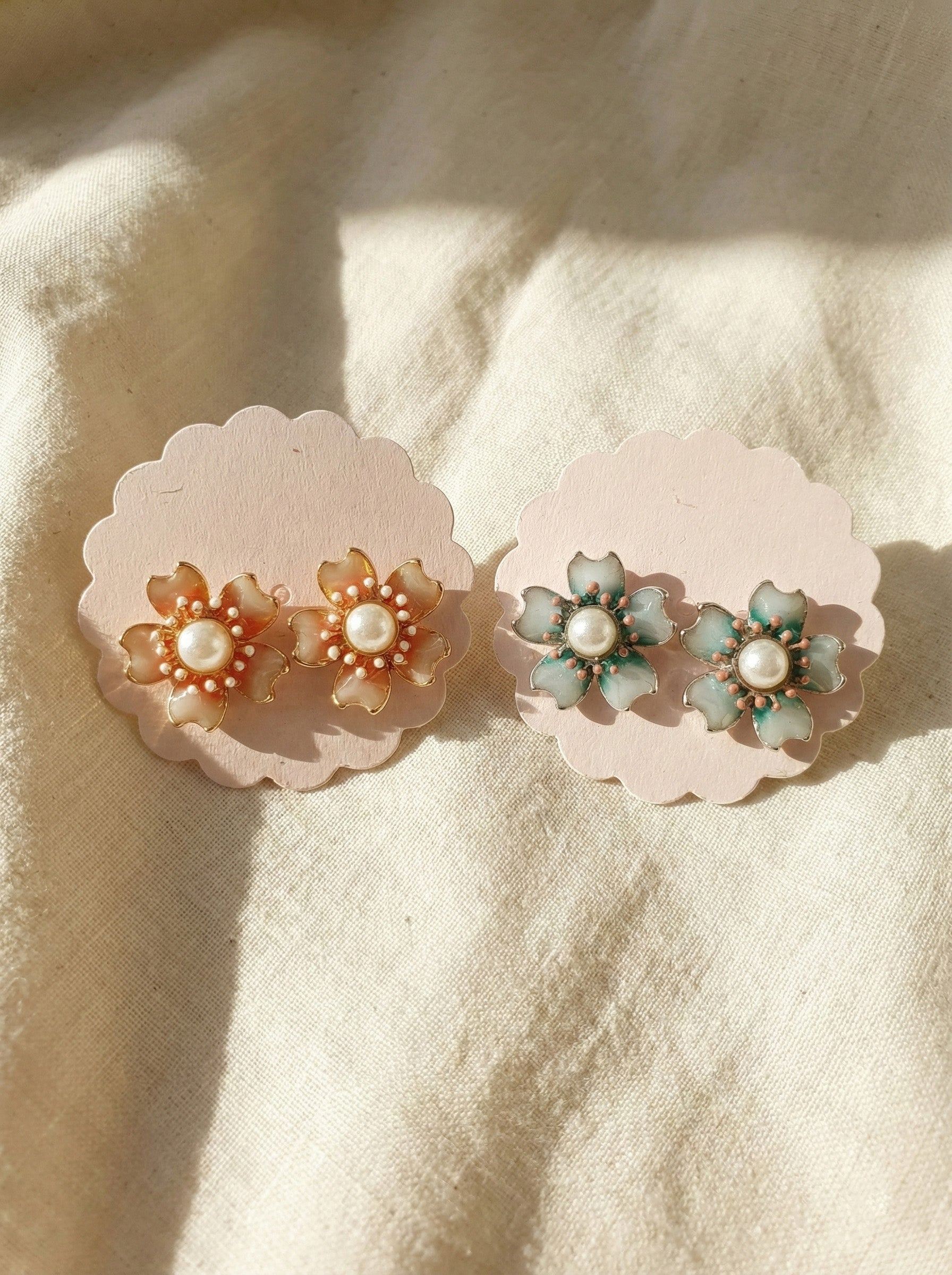 Two pairs of handmade Korean vintage flower earrings in mint green and peach coral on cream fabric with natural lighting