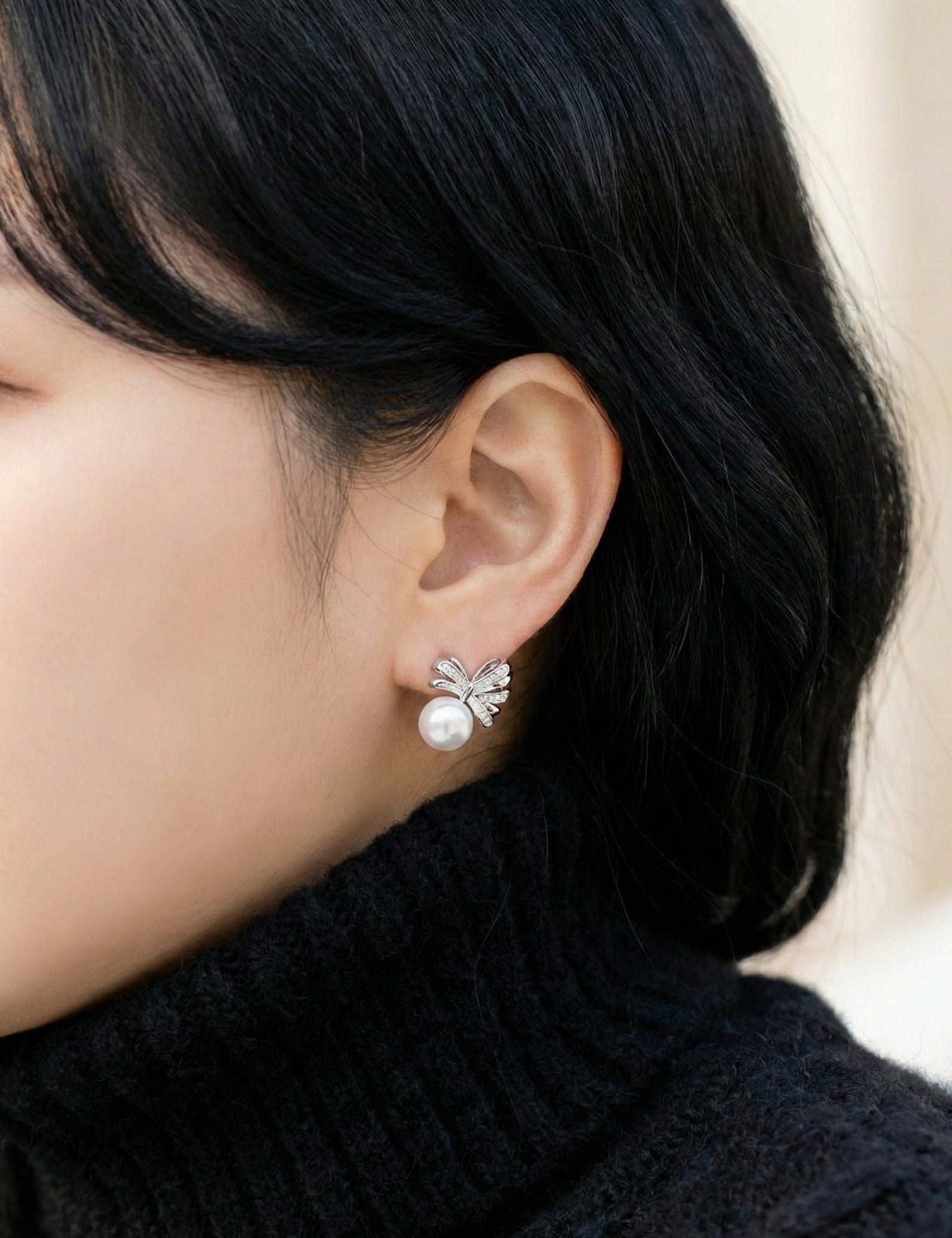 Woman wearing elegant silver ribbon bow pearl stud earrings with cubic zirconia, side view