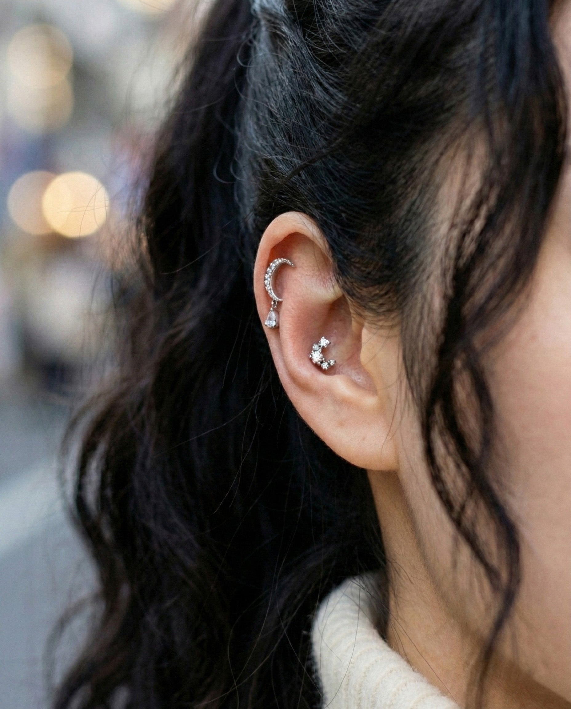 Crescent moon teardrop dangle cartilage piercing worn on inner conch and outer conch with natural outdoor lighting
