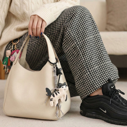 cream leather cat bag charm with sparkly rhinestone ribbon attached to ivory hobo bag