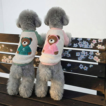 Two gray poodles wearing mint and pink bear fleece dog shirts sitting on wooden bench outdoors