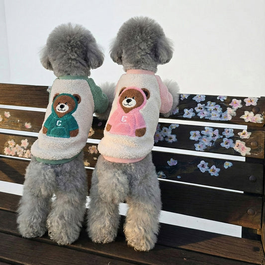 Two gray poodles wearing mint and pink bear fleece dog shirts sitting on wooden bench outdoors