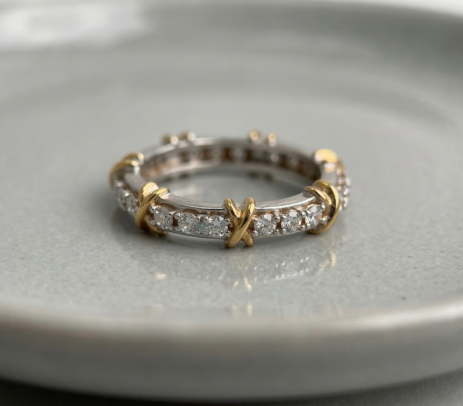 925 sterling silver two-tone eternity band with gold X-cross accents and round cubic zirconia pavé, placed flat on a gray ceramic dish — full product view