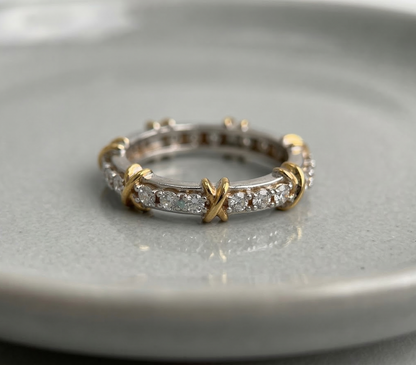 925 sterling silver two-tone eternity band with gold X-cross accents and round cubic zirconia pavé, placed flat on a gray ceramic dish — full product view