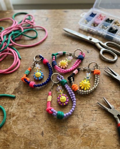  Kidcore Y2K handmade smiley flower beaded keychain 8ttitto8, all 4 colorways flat lay on artisan workbench with tools and rope.

