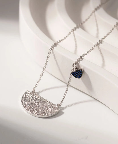 Product flat lay — Textured hammered half-moon pendant close-up, sterling silver 925 tarnish-free necklace detail.