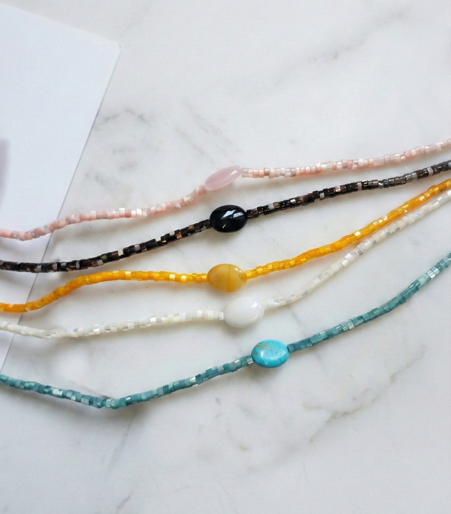 Five colorful gemstone choker necklaces with shell heishi beads in turquoise, black, yellow, white, and pink