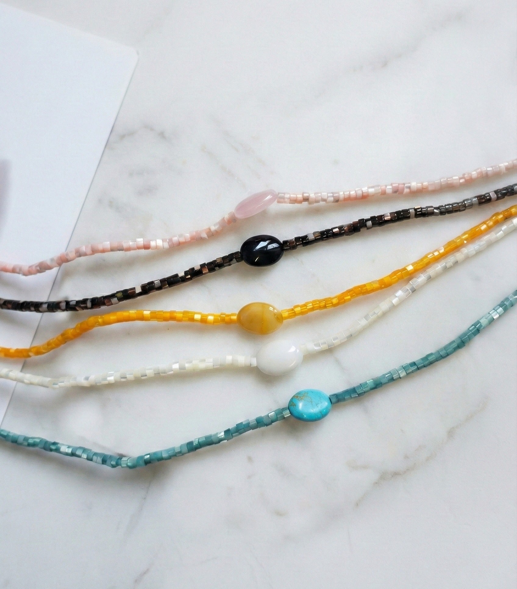 Five colorful gemstone choker necklaces with shell heishi beads in turquoise, black, yellow, white, and pink