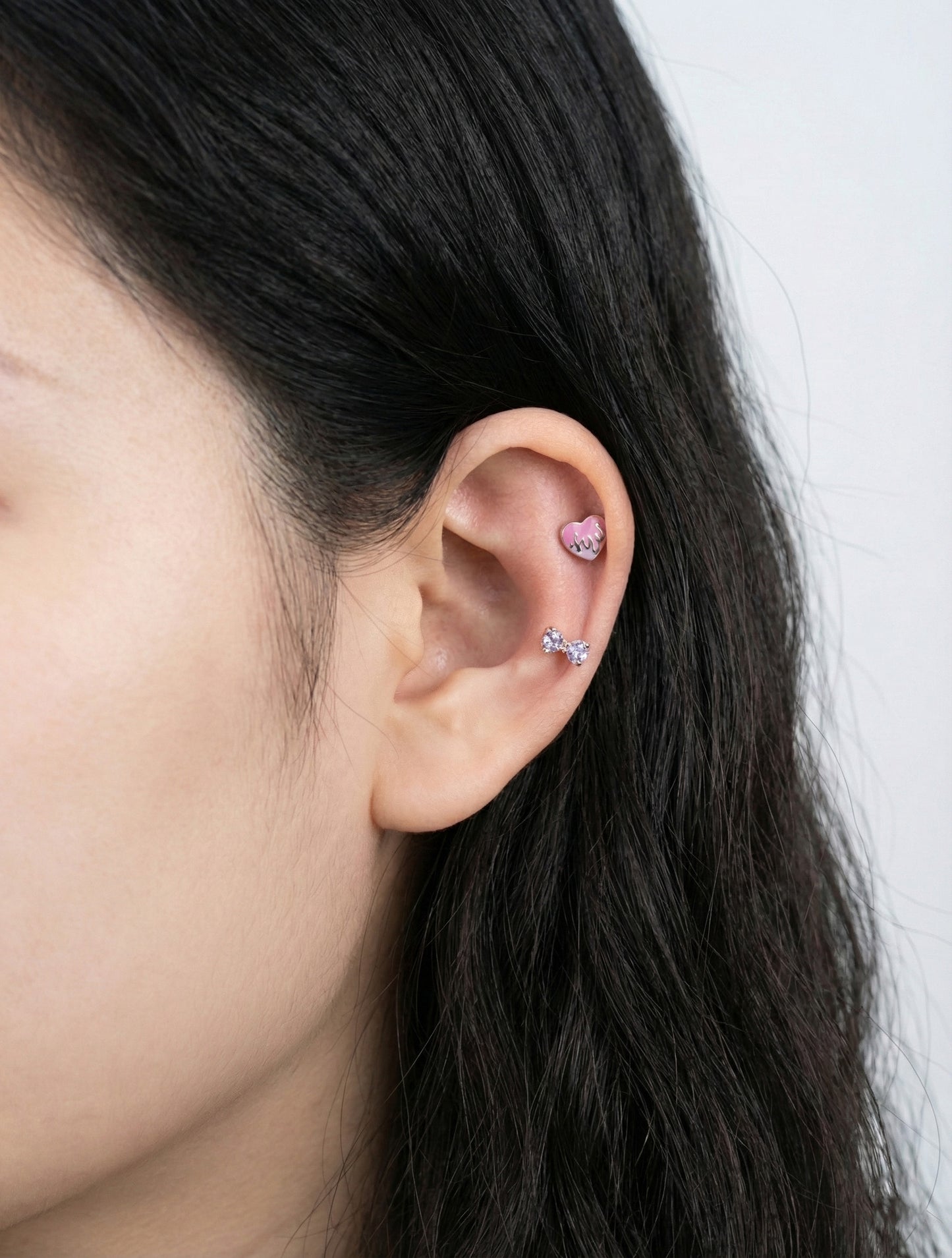 Pink melting heart piercing worn on inner conch and CZ stud on lobe showing Y2K ear styling