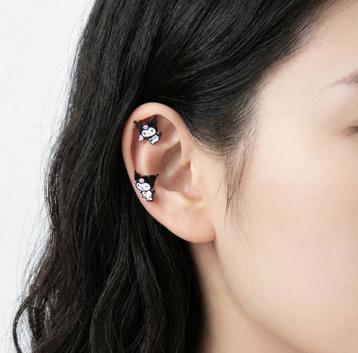 Kuromi character enamel stud earrings on ear showing helix and lobe placement with surgical steel posts