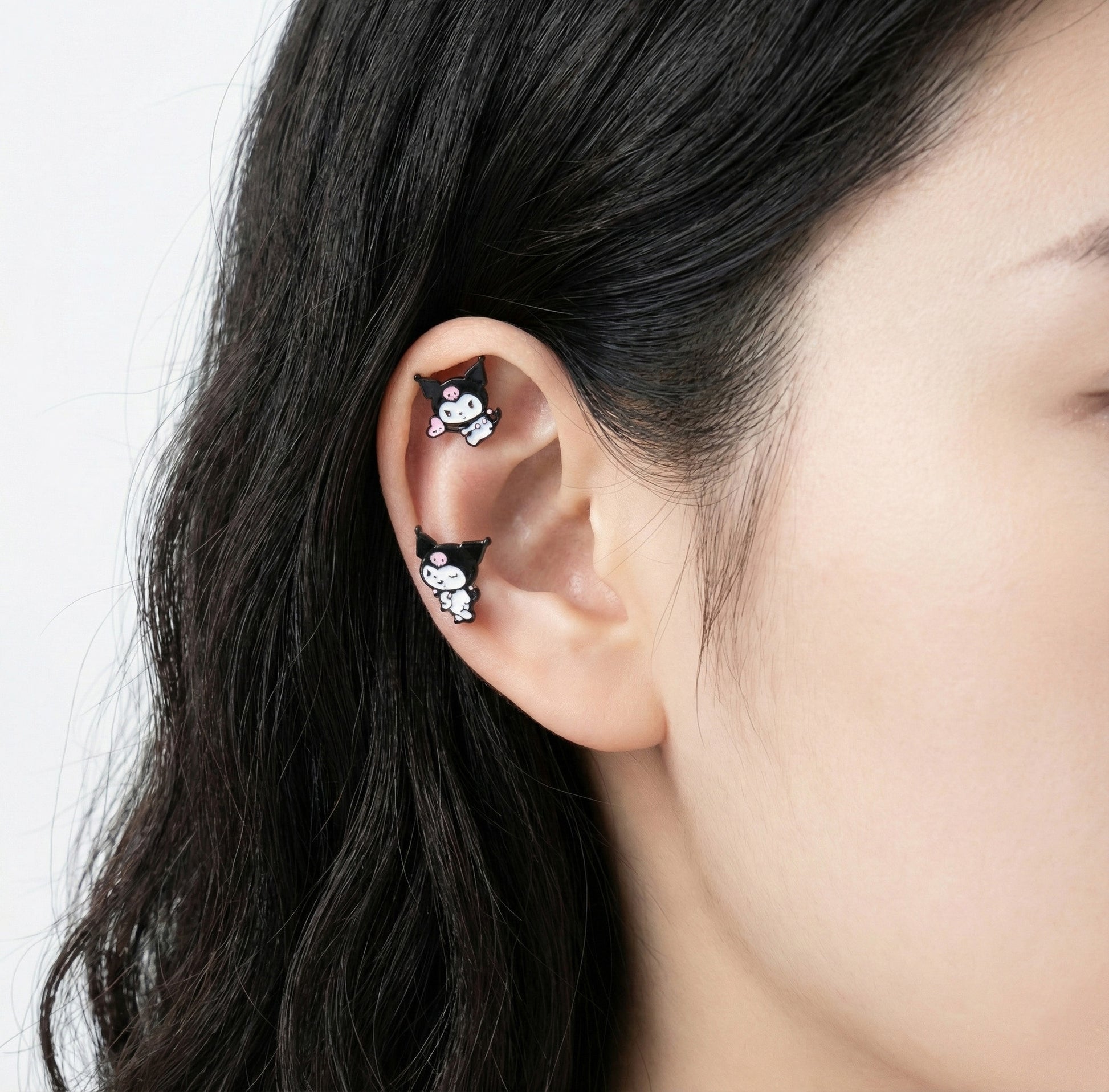 Kuromi character enamel stud earrings on ear showing helix and lobe placement with surgical steel posts