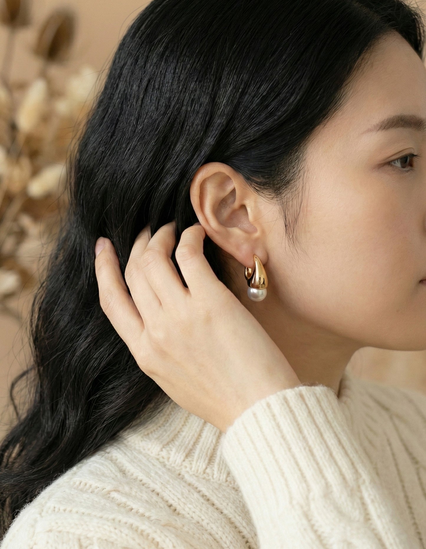 Model wearing gold and silver teardrop pearl huggie earrings with cream knit sweater side profile view