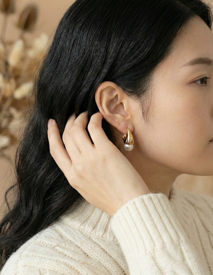 Model wearing gold and silver teardrop pearl huggie earrings with cream knit sweater side profile view