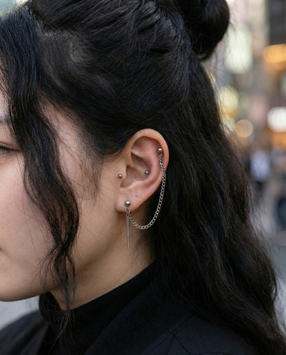 Woman wearing chain connected piercing linking helix and lobe with stick drop charm