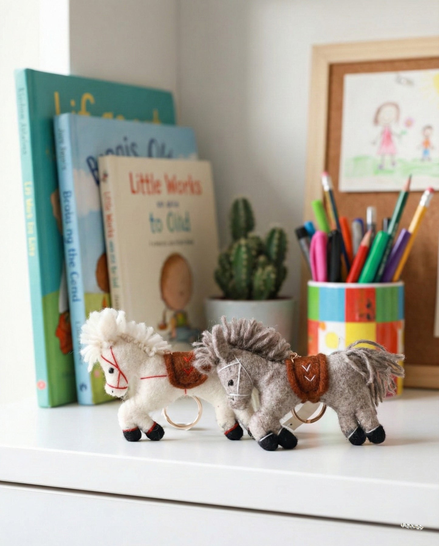 Handmade wool felt horse keychain in white and grey displayed on desk with books and stationery
