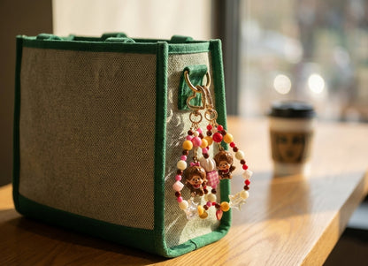 Monchhichi beaded keychain with pink and yellow gingham cube beads attached to green canvas tote bag on cafe table