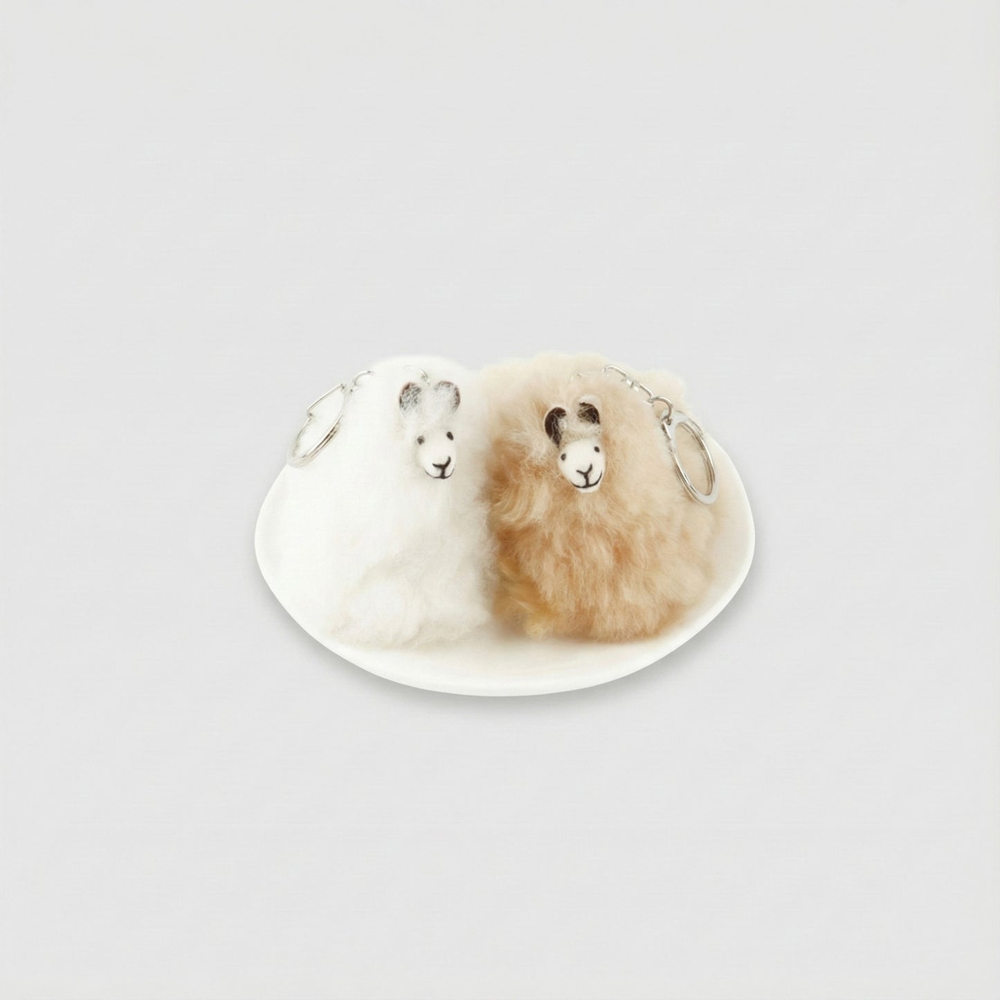 Two real alpaca fur keychains in white and beige on a ceramic plate