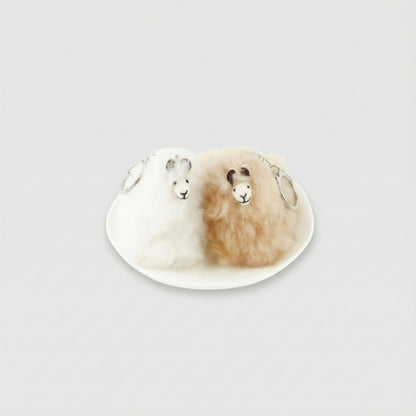 Two real alpaca fur keychains in white and beige on a ceramic plate