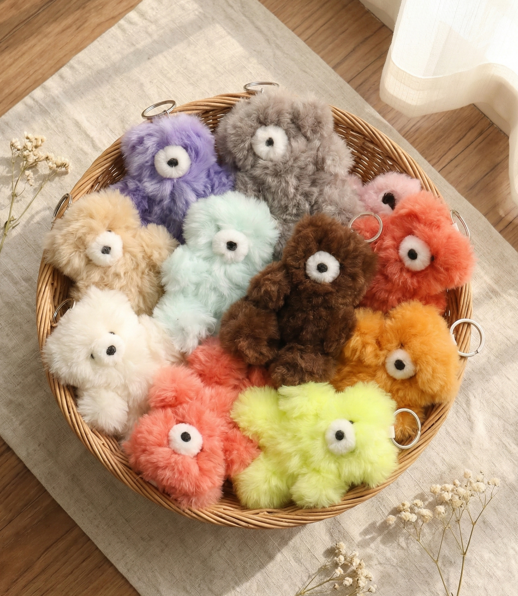 Fluffy alpaca wool bear keyrings in 10 colors including purple, gray, pink, coral, mint, brown, orange, yellow-green, beige and white, arranged in a round wicker basket on linen cloth