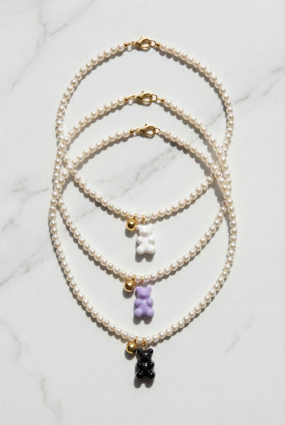 Three Swarovski pearl gummy bear necklaces in white, lavender, and black displayed on marble surface