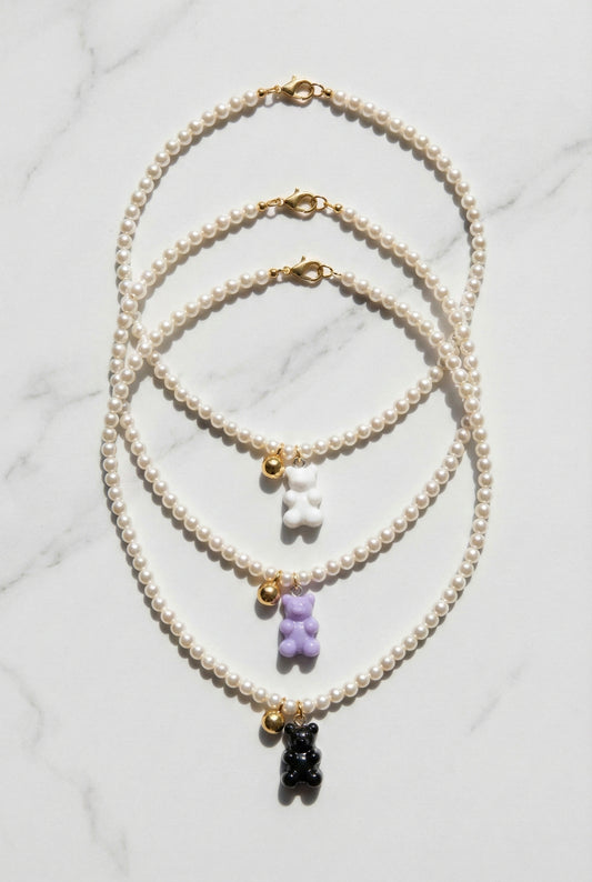 Three Swarovski pearl gummy bear necklaces in white, lavender, and black displayed on marble surface