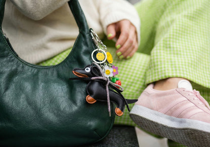 Black leather Dachshund keychain with crystal ribbon attached to green bag with colorful charms and smiley face accessories