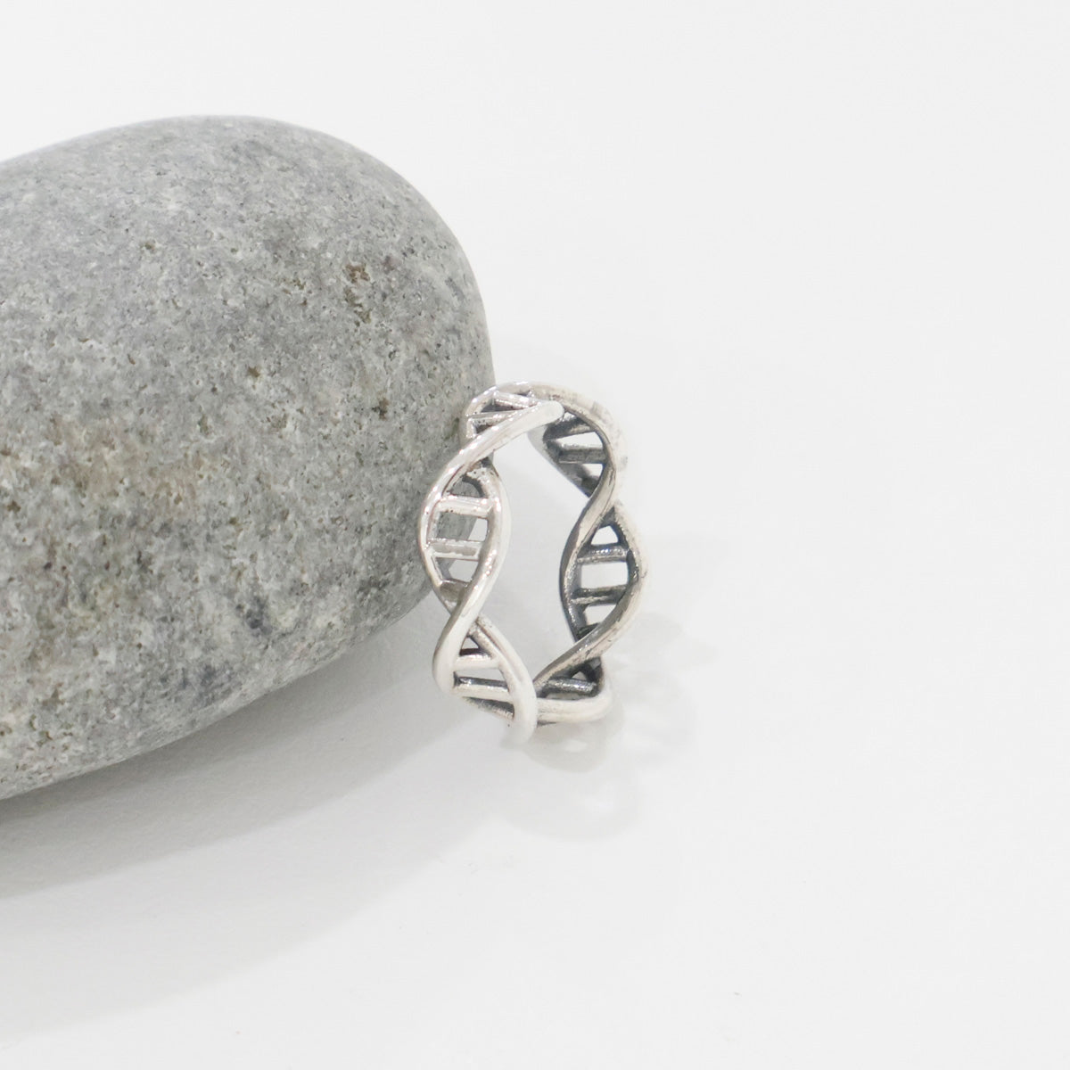 Sterling silver DNA helix ring leaning against a smooth grey stone, minimalist close-up