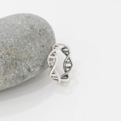 Sterling silver DNA helix ring leaning against a smooth grey stone, minimalist close-up