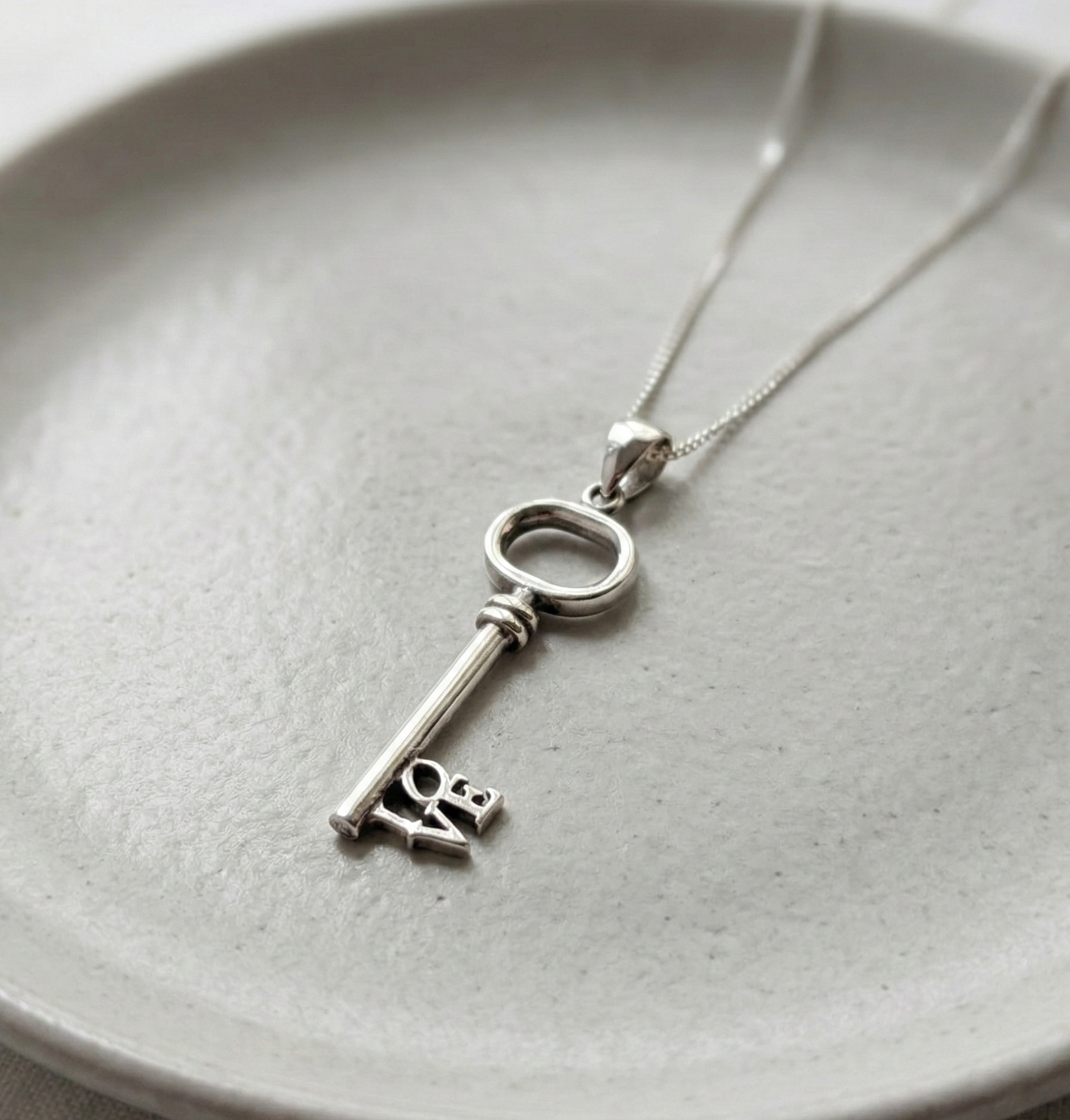 Flat lay of 925 Sterling Silver LOVE key necklace on a minimalist grey ceramic plate.