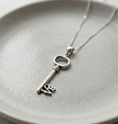 Flat lay of 925 Sterling Silver LOVE key necklace on a minimalist grey ceramic plate.