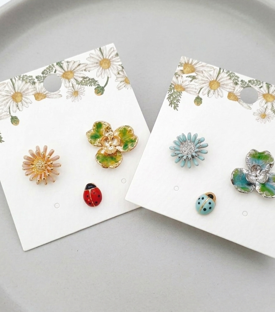 Two sets of handmade asymmetrical stud earrings (Retro Red and Fresh Mint) with daisy, ladybug, and clover designs displayed on floral backing cards.
