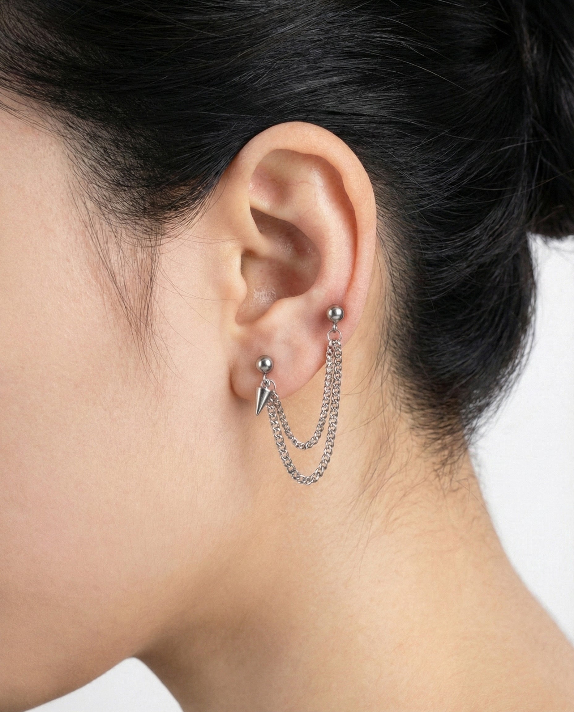 Double chain piercing connecting two lobe piercings with spike charm detail