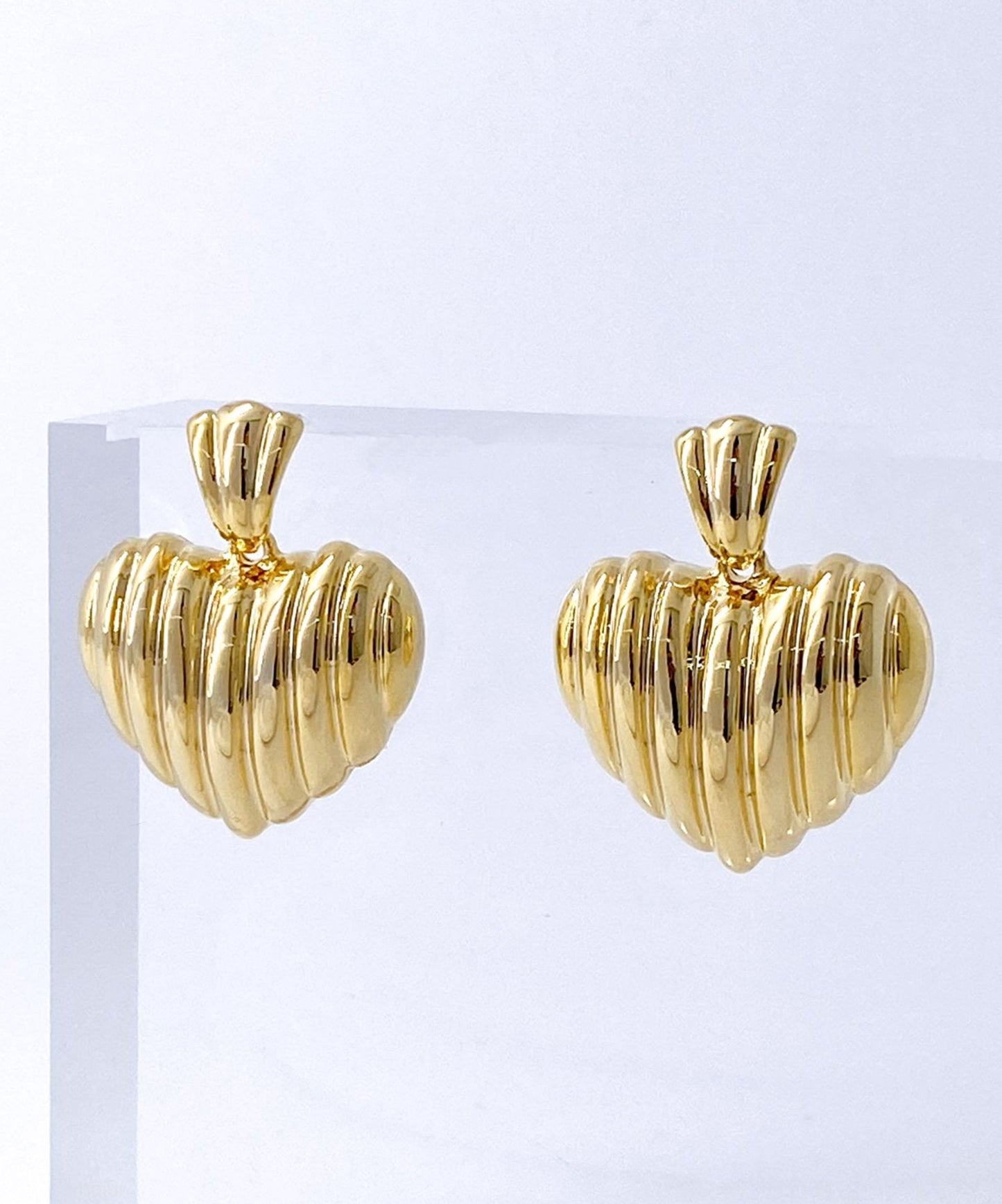 Gold ribbed heart stud earrings on white stone texture background