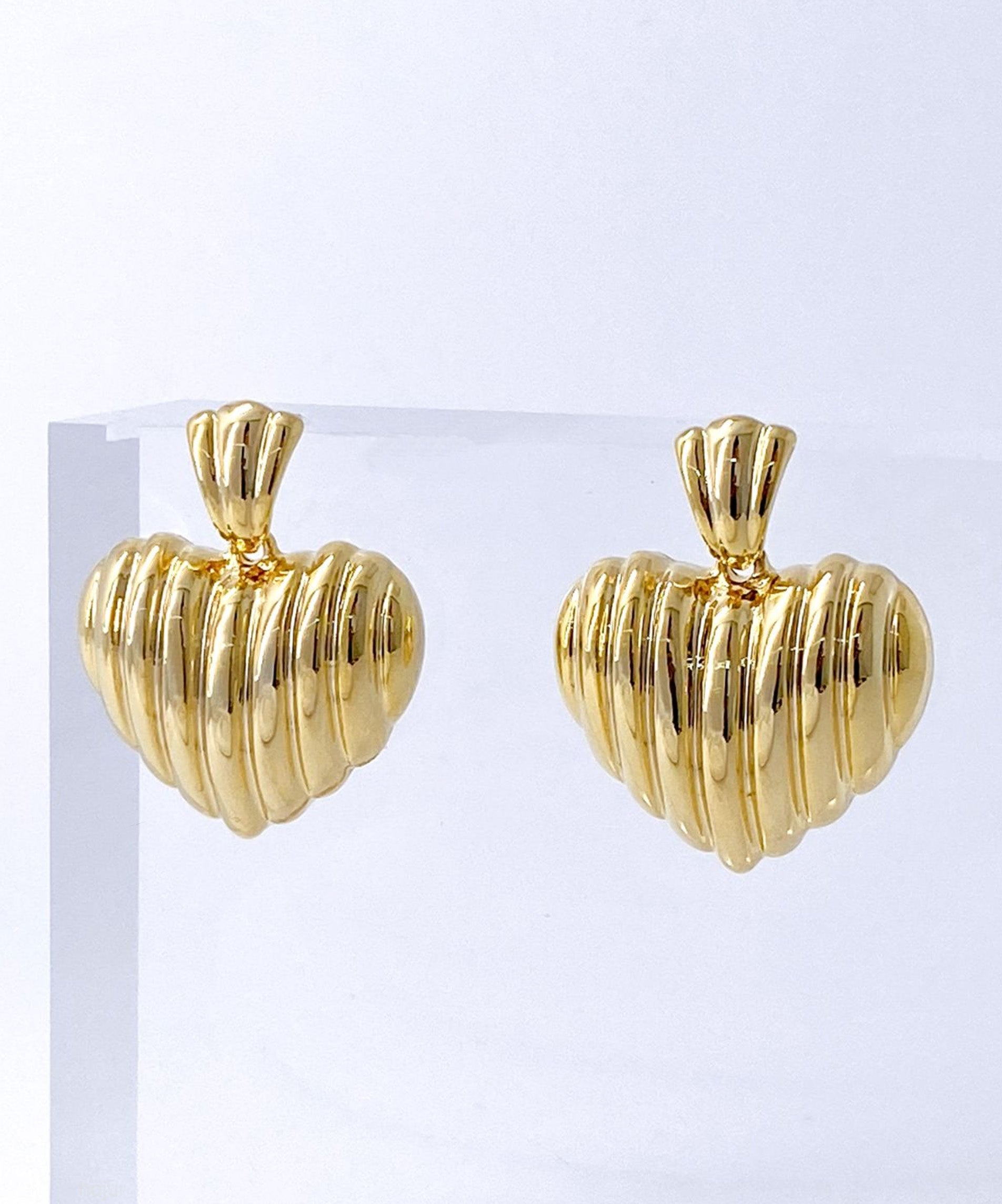 Gold ribbed heart stud earrings on white stone texture background