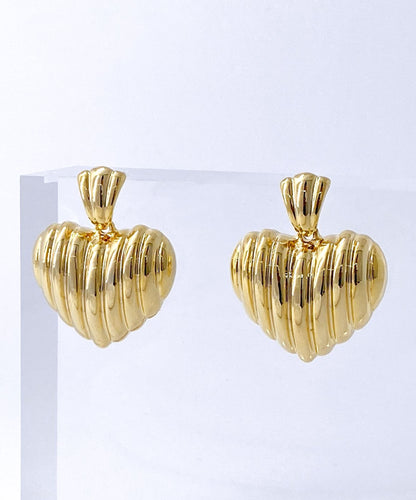 Gold ribbed heart stud earrings on white stone texture background