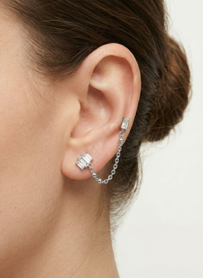 Close-up of a woman's ear wearing a silver Baguette CZ Chain Double Stud Earring made of surgical steel, featuring clear rectangular stones connected by a delicate chain.