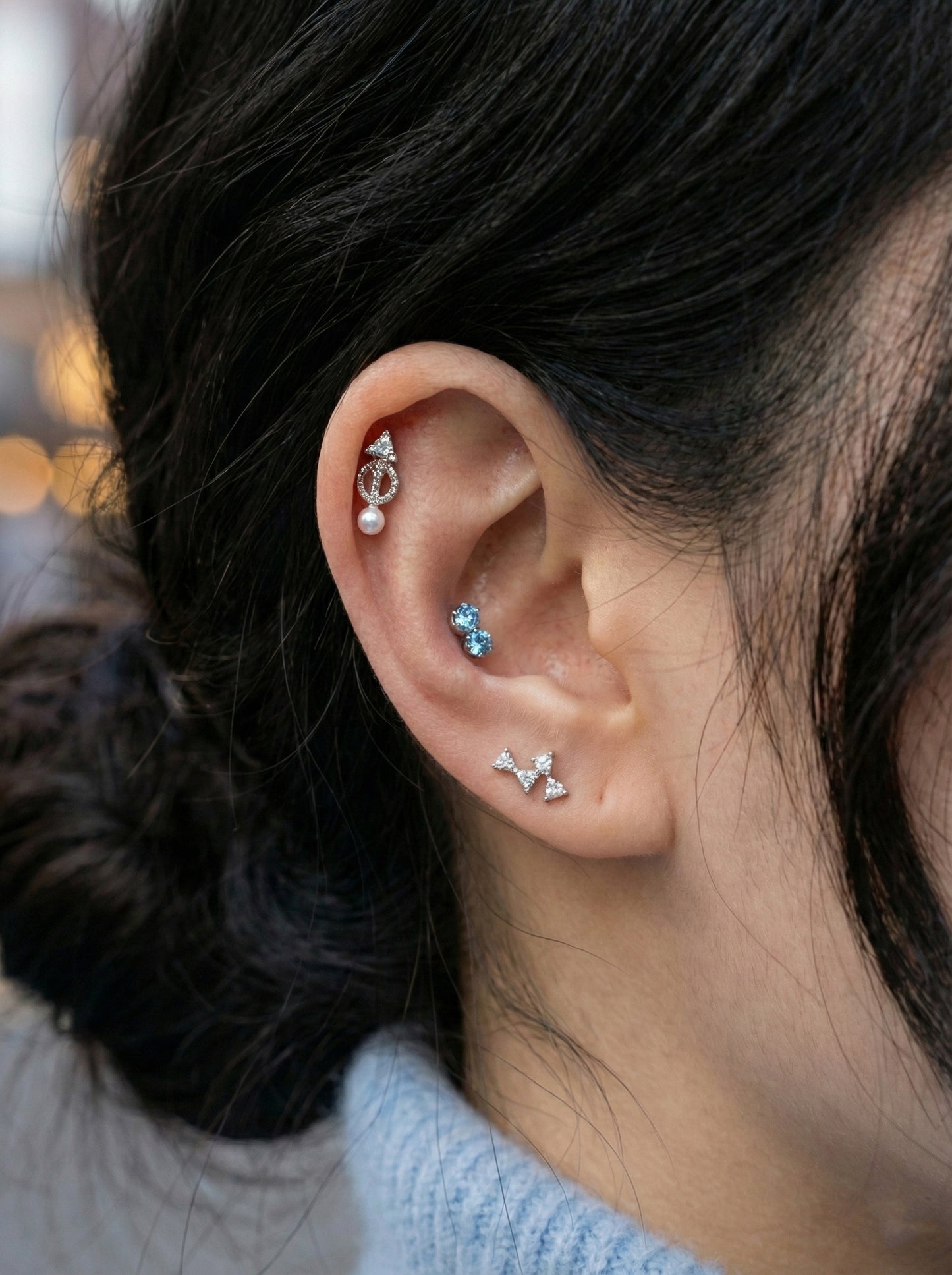 Close-up of vintage arrow-shaped CZ pearl drop helix stud worn on cartilage with layered cubic zirconia earrings