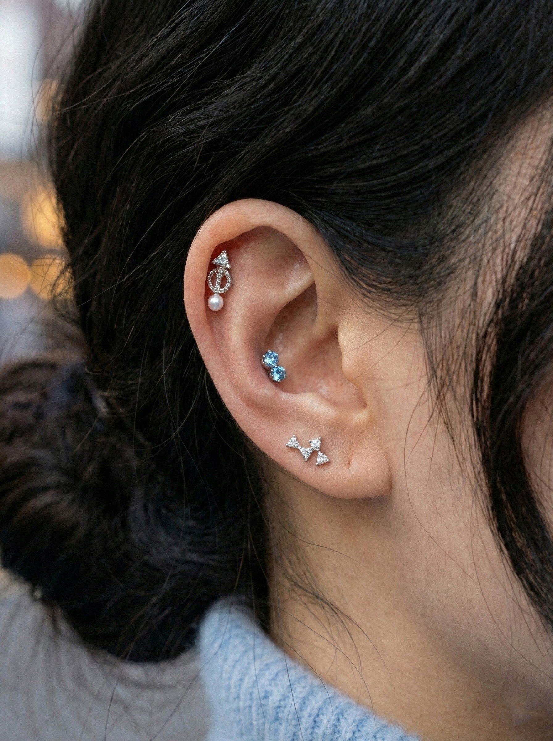 Close-up of vintage arrow-shaped CZ pearl drop helix stud worn on cartilage with layered cubic zirconia earrings