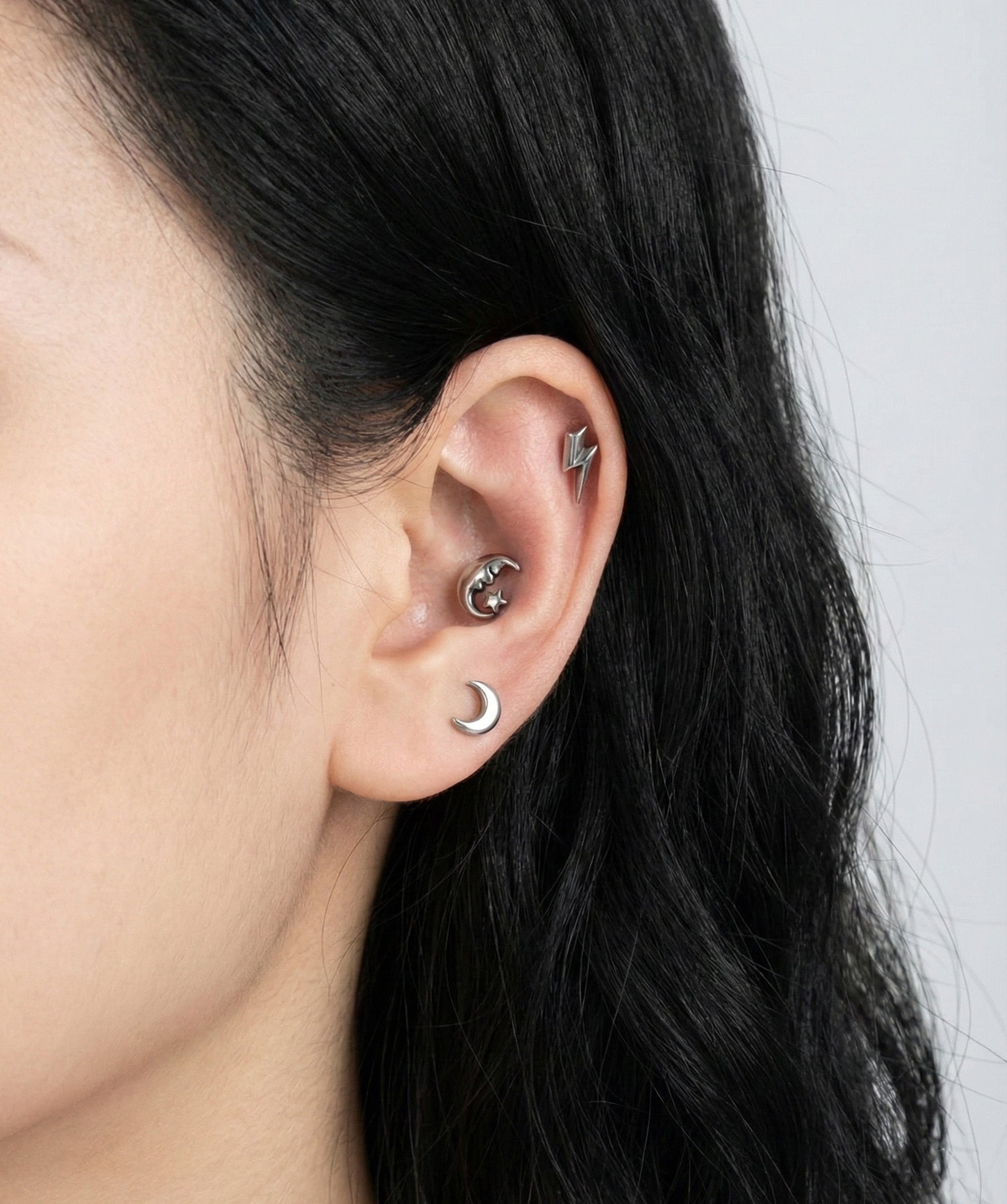 Celestial surgical steel barbell studs layered on ear - moon, crescent, lightning bolt designs