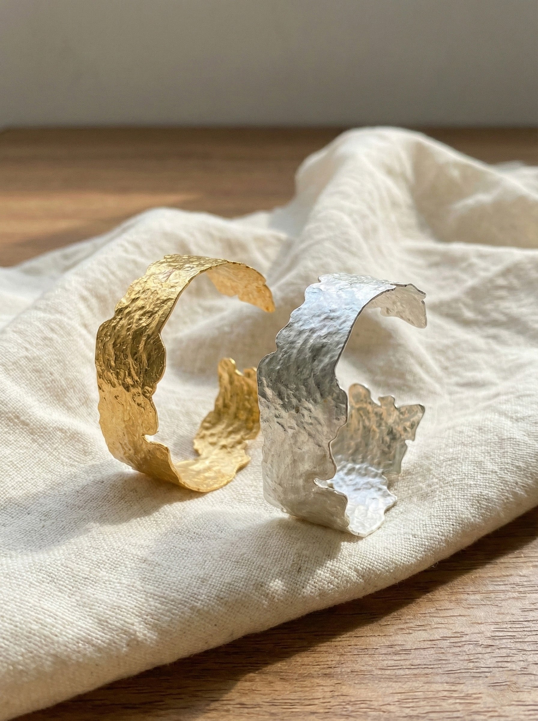Gold and silver hammered wide cuff bangles on linen fabric - artisan textured brass jewelry
