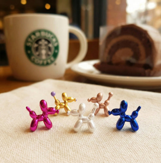Five colorful balloon dog earrings displayed on cafe table - fuchsia pink, blue, gold, white and rose gold metallic finish
