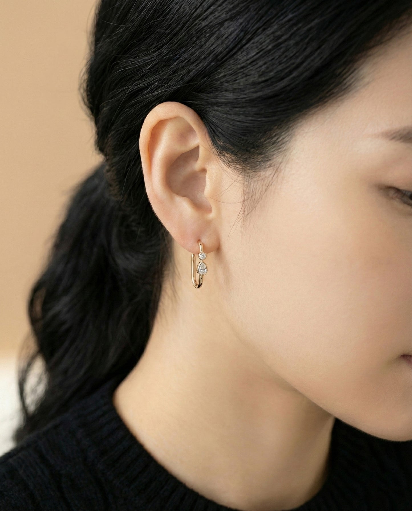Model wearing gold bezel-set teardrop cubic zirconia U-shaped hoop earrings on beige background