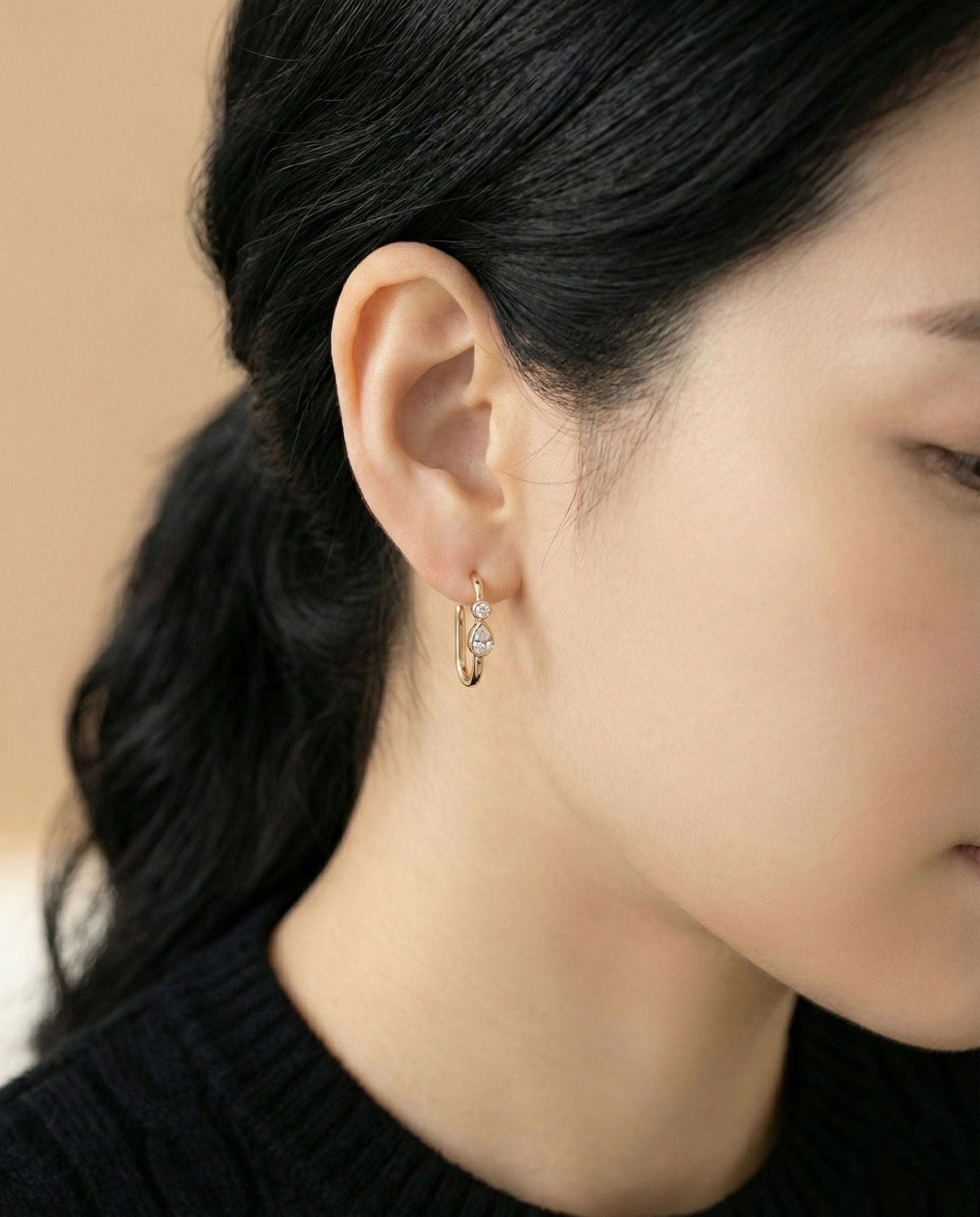 Model wearing gold bezel-set teardrop cubic zirconia U-shaped hoop earrings on beige background