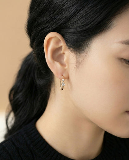Model wearing gold bezel-set teardrop cubic zirconia U-shaped hoop earrings on beige background