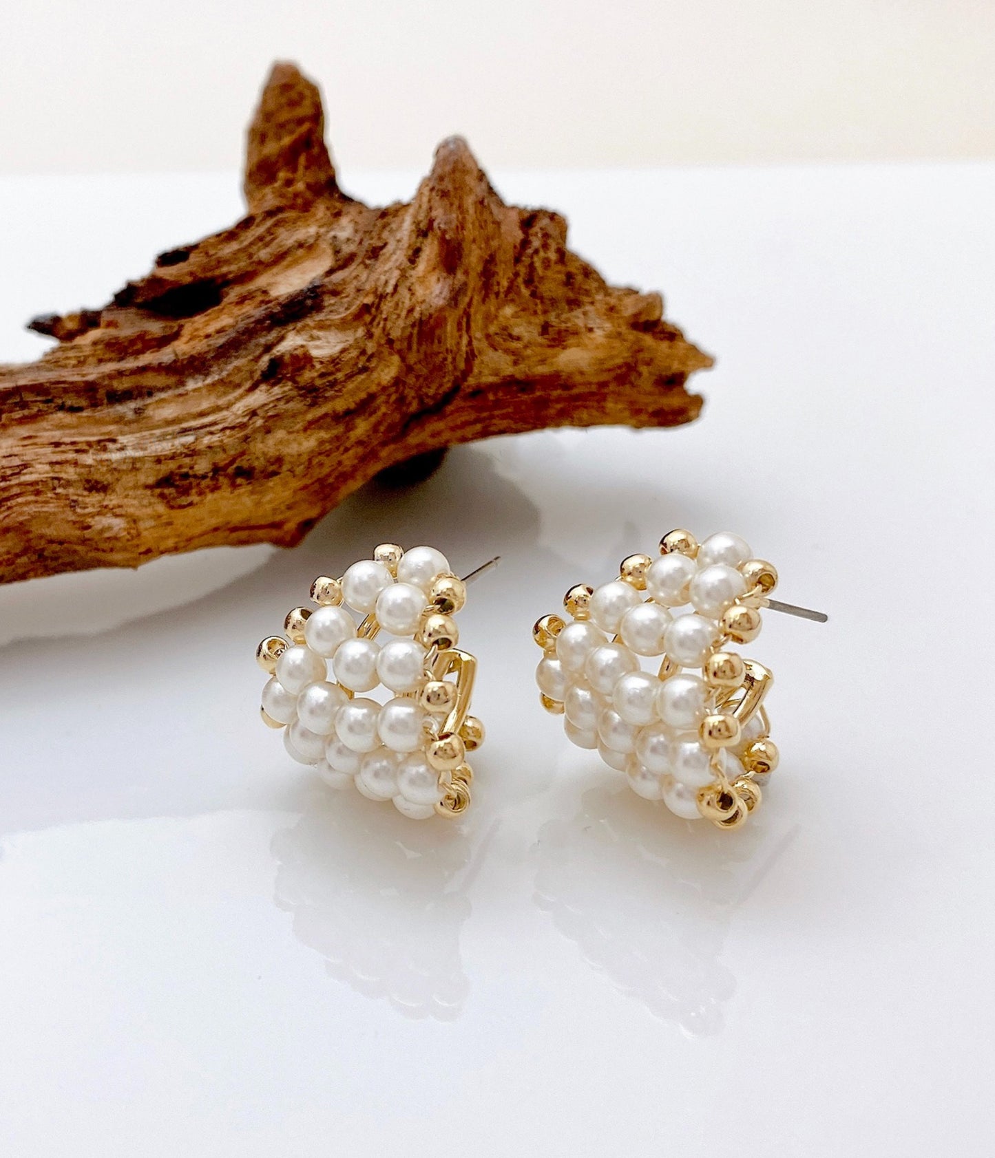 Chunky pearl heart C-hoop earrings in gold displayed on natural wood branch