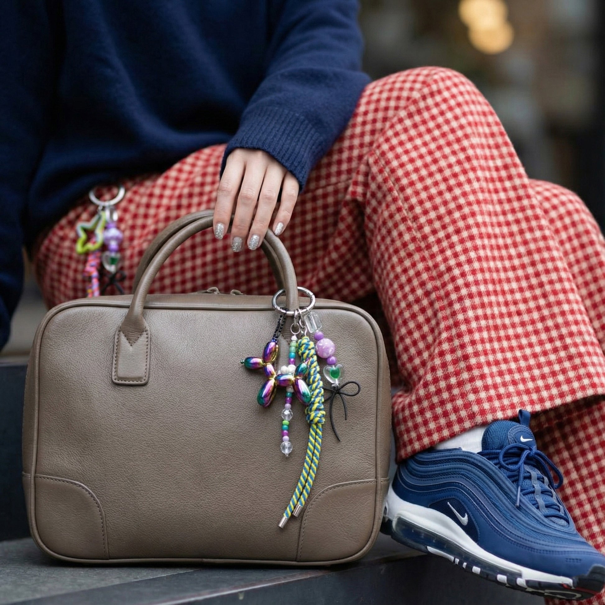 Rainbow iridescent balloon dog keychain on beige leather bag with checkered pants styling