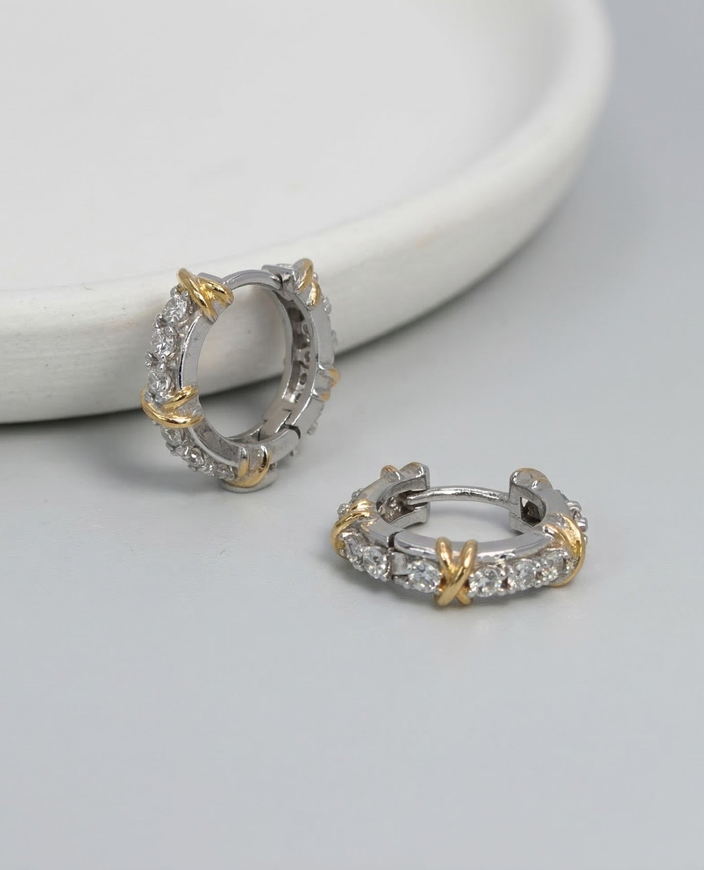 Two-tone CZ huggie hoop earrings with gold criss-cross X detail on white marble surface 